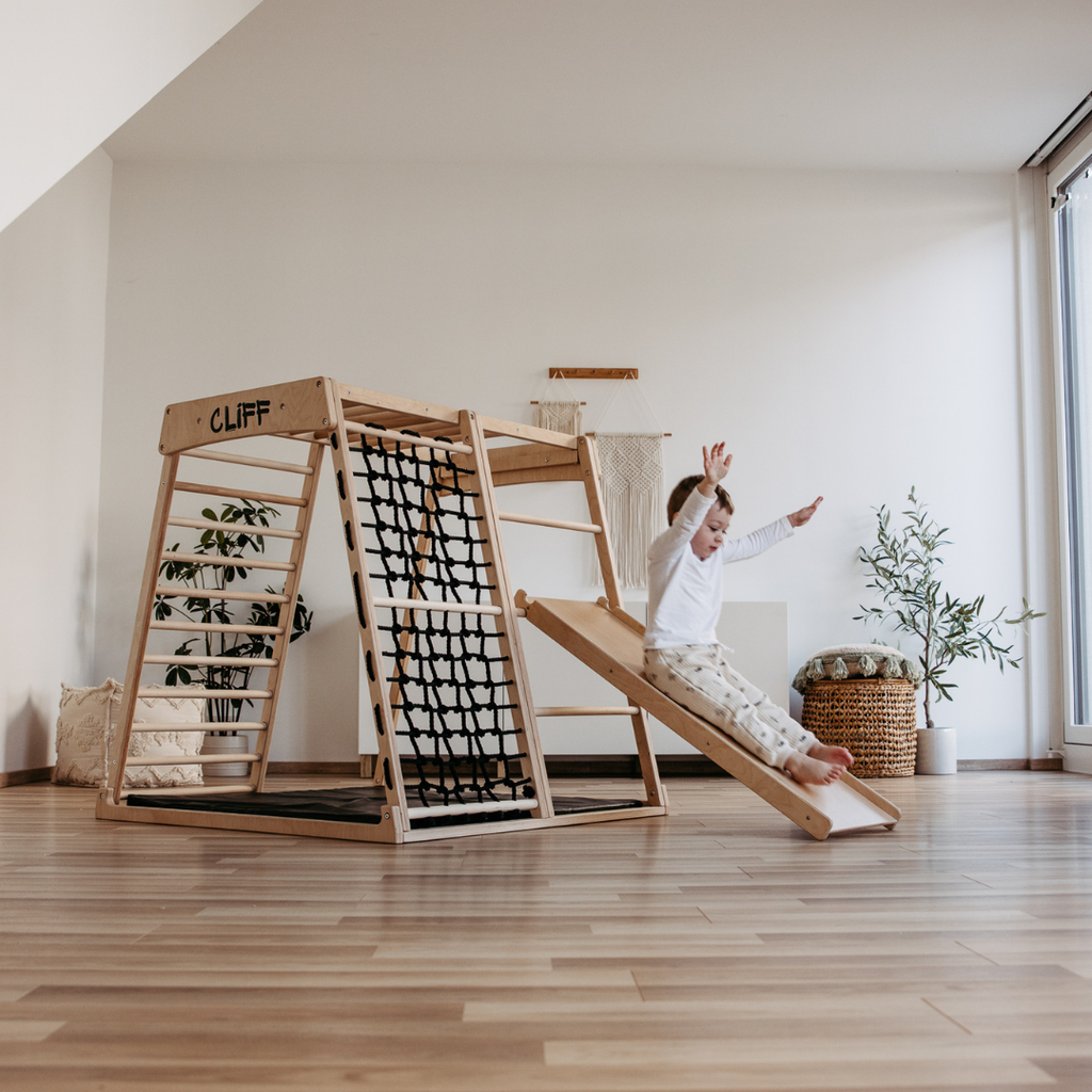Kind rutscht mit Händen nach oben auf CLIFF Rutschrampe aus Naturholz im Kinderzimmer