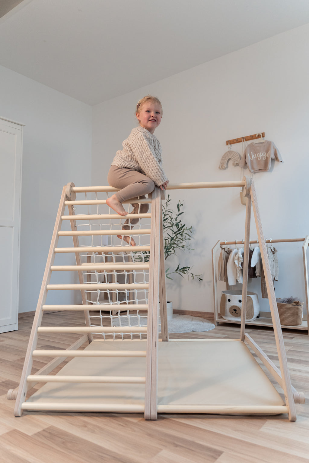 Kind sitzt oben auf dem CLIFF FLEX White Edition Klettergerüst mit Premium-Matte im Kinderzimmer