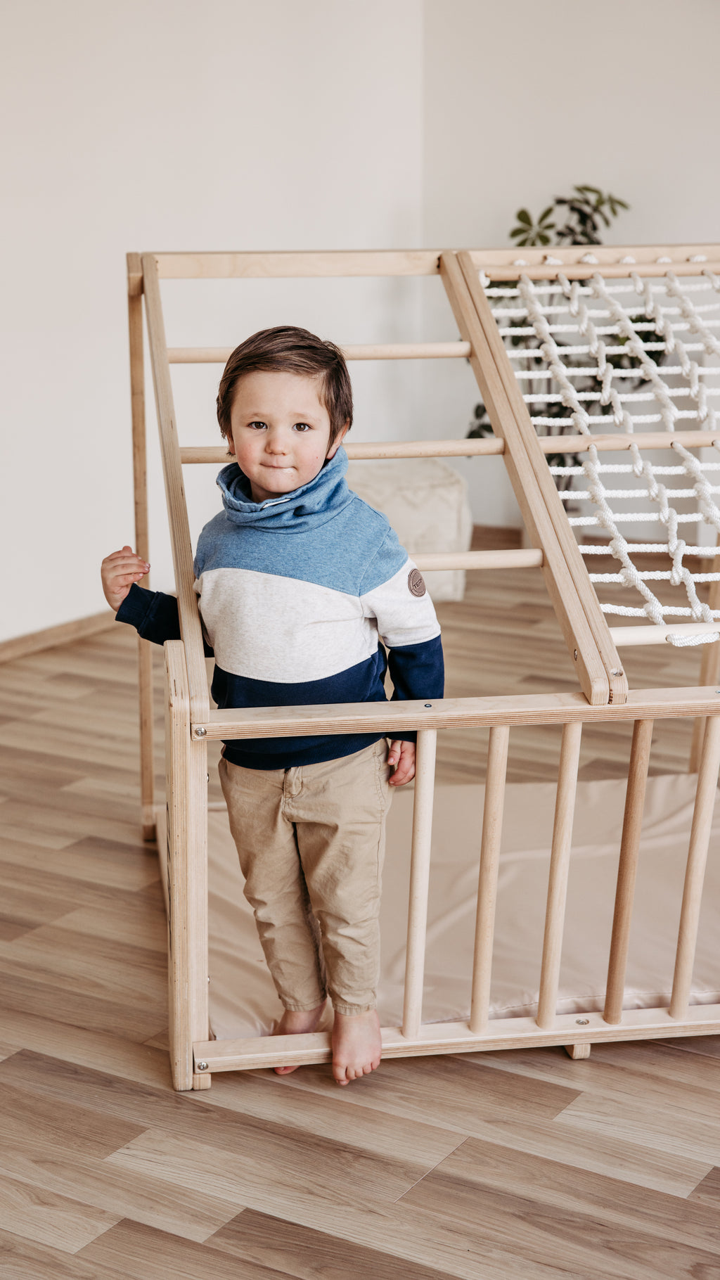 Kind steht am CLIFF PRO White Edition Klettergerüst mit Holzsprossen und Kletternetz