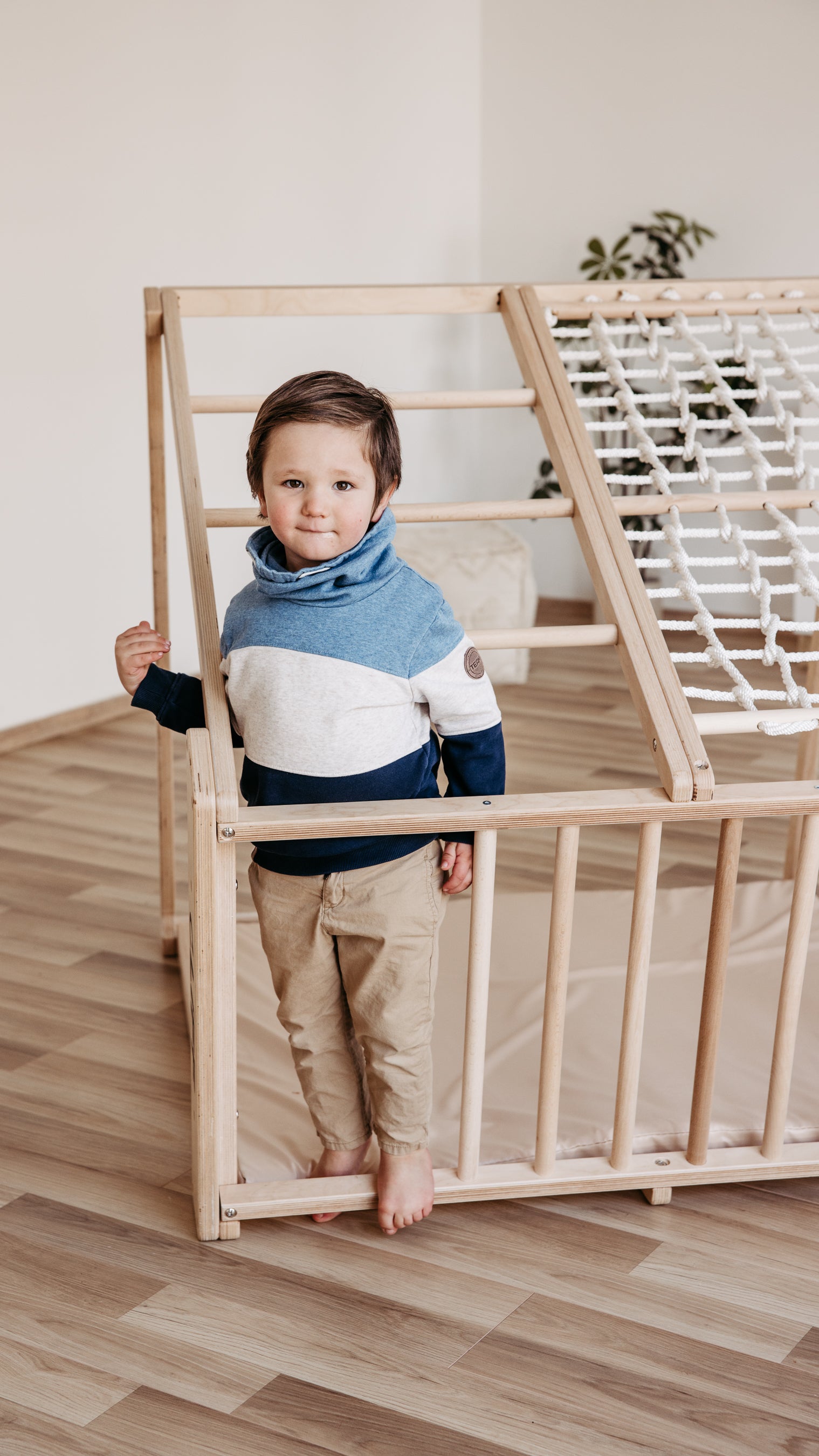 Kind steht am CLIFF PRO White Edition Klettergerüst mit Holzsprossen und Kletternetz