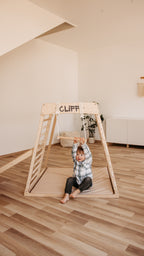 Kind schwingt am CLIFF Holztrapez aus Naturholz im Kinderzimmer