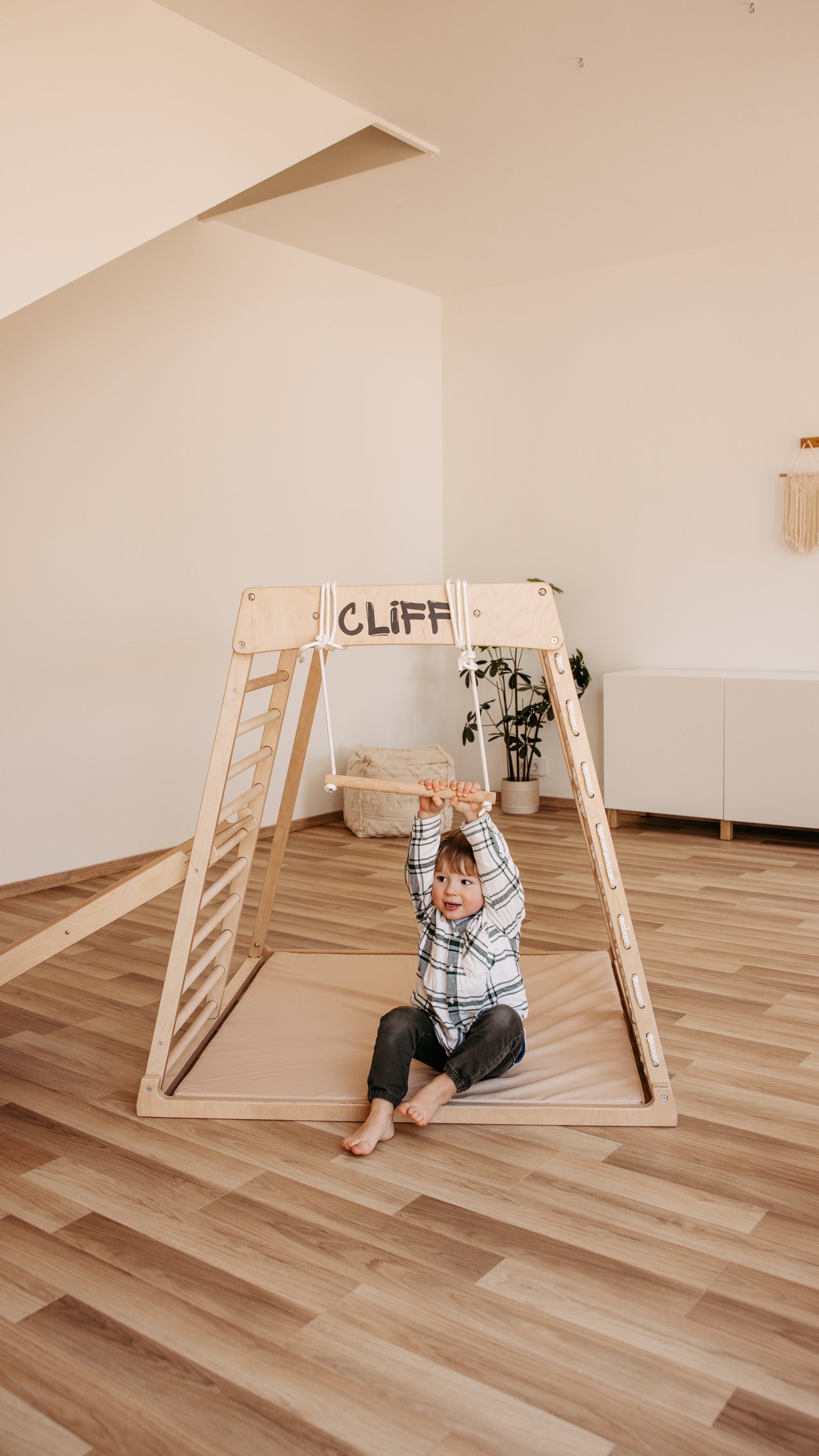 Kind schwingt am CLIFF Holztrapez aus Naturholz im Kinderzimmer