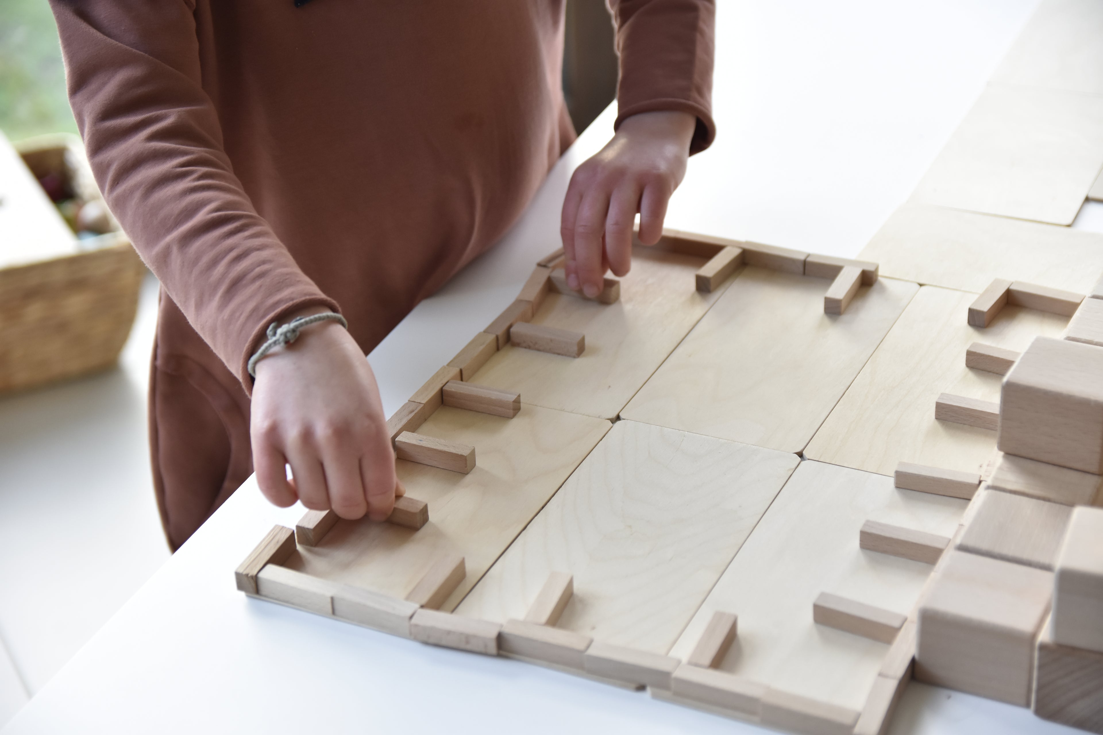 Kind baut mit Just Blocks BASIC Small eine flache Bauwelt aus Holzelementen