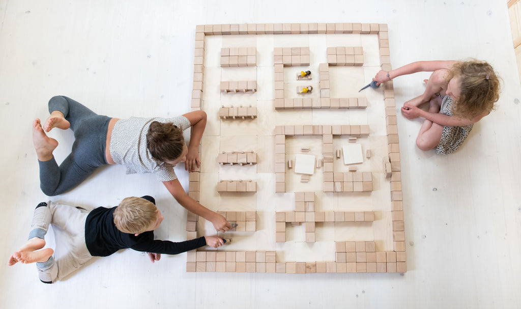Drei Kinder bauen mit Just Blocks BASIC Big eine grosse Bauwelt aus Holzelementen