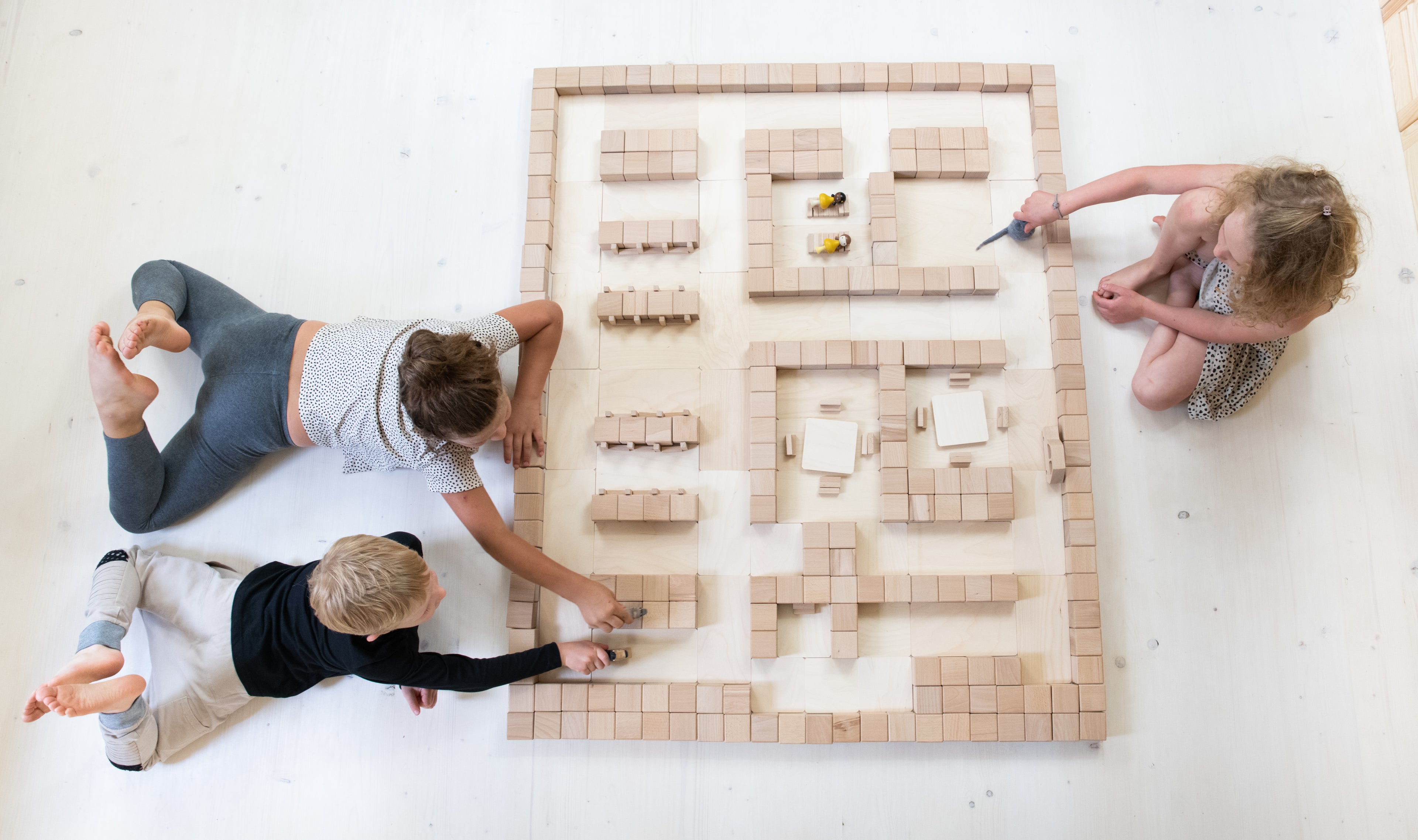 Drei Kinder bauen mit Just Blocks BASIC Big eine grosse Bauwelt aus Holzelementen