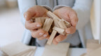 Hände halten Stäbe aus dem Just Blocks BASIC Small Holz-Lernsystem
