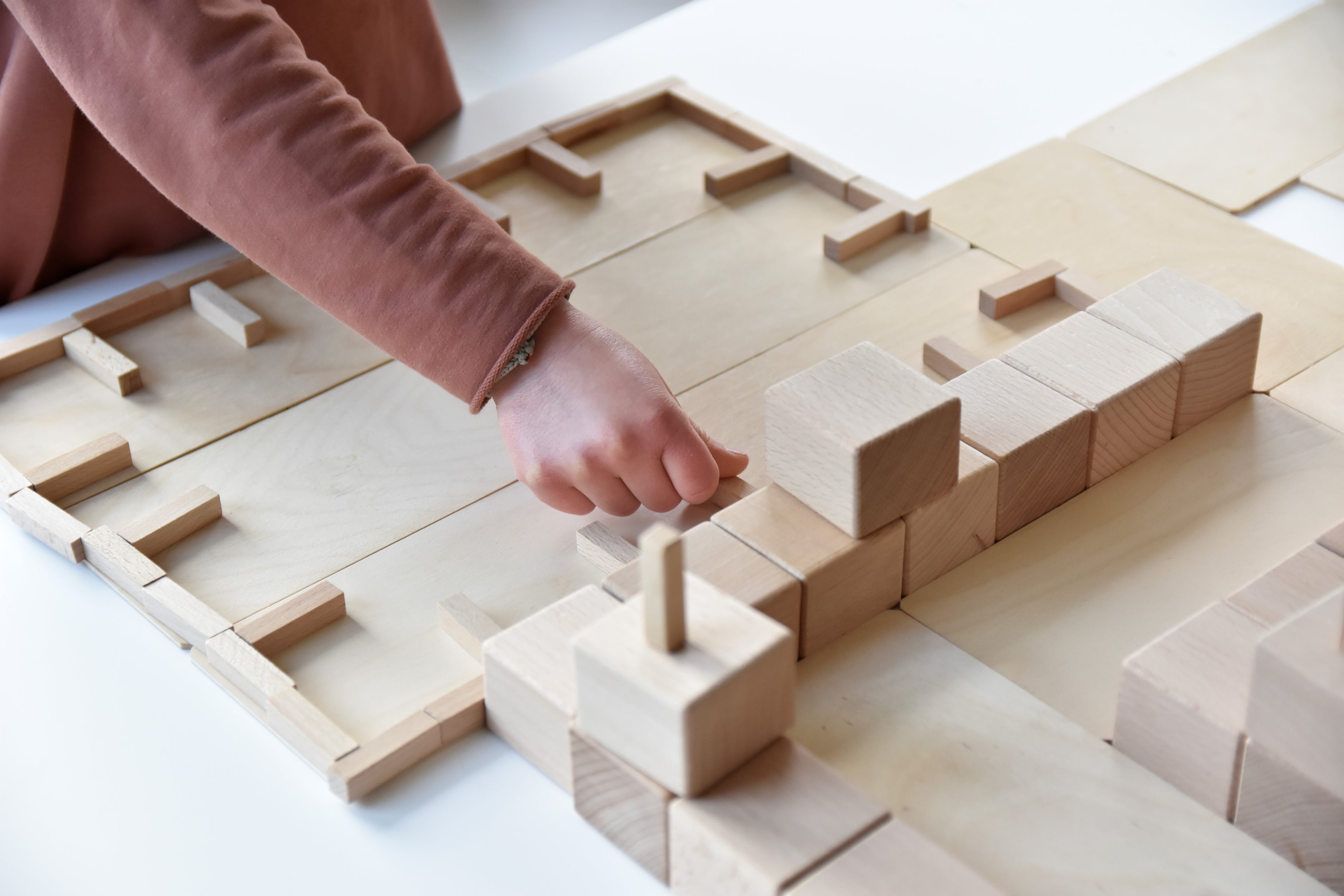 Kind baut mit Just Blocks BASIC Medium eine flache Bauwelt aus Holzelementen